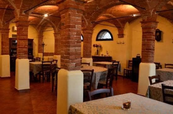 La sala: volte e colonne di mattoni, i tavoli apparecchiati e una finestra a lunetta